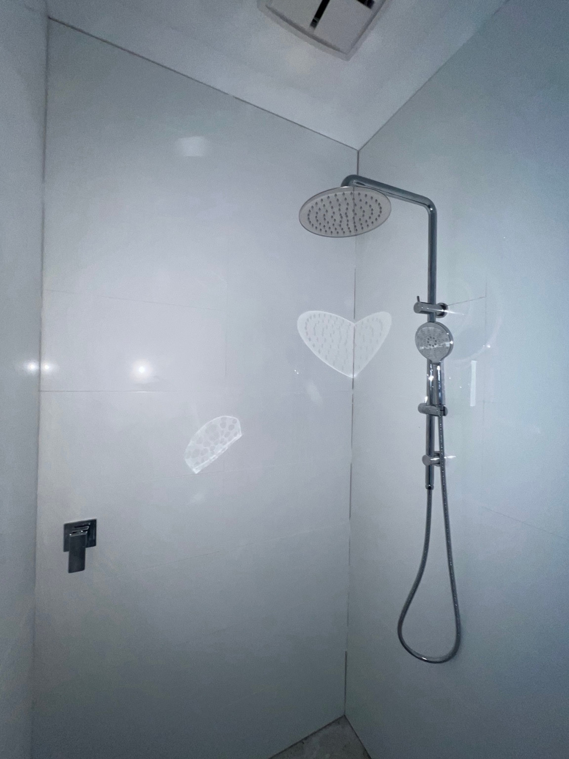 Chrome rainfall shower and handheld sprayer against white tiles.
