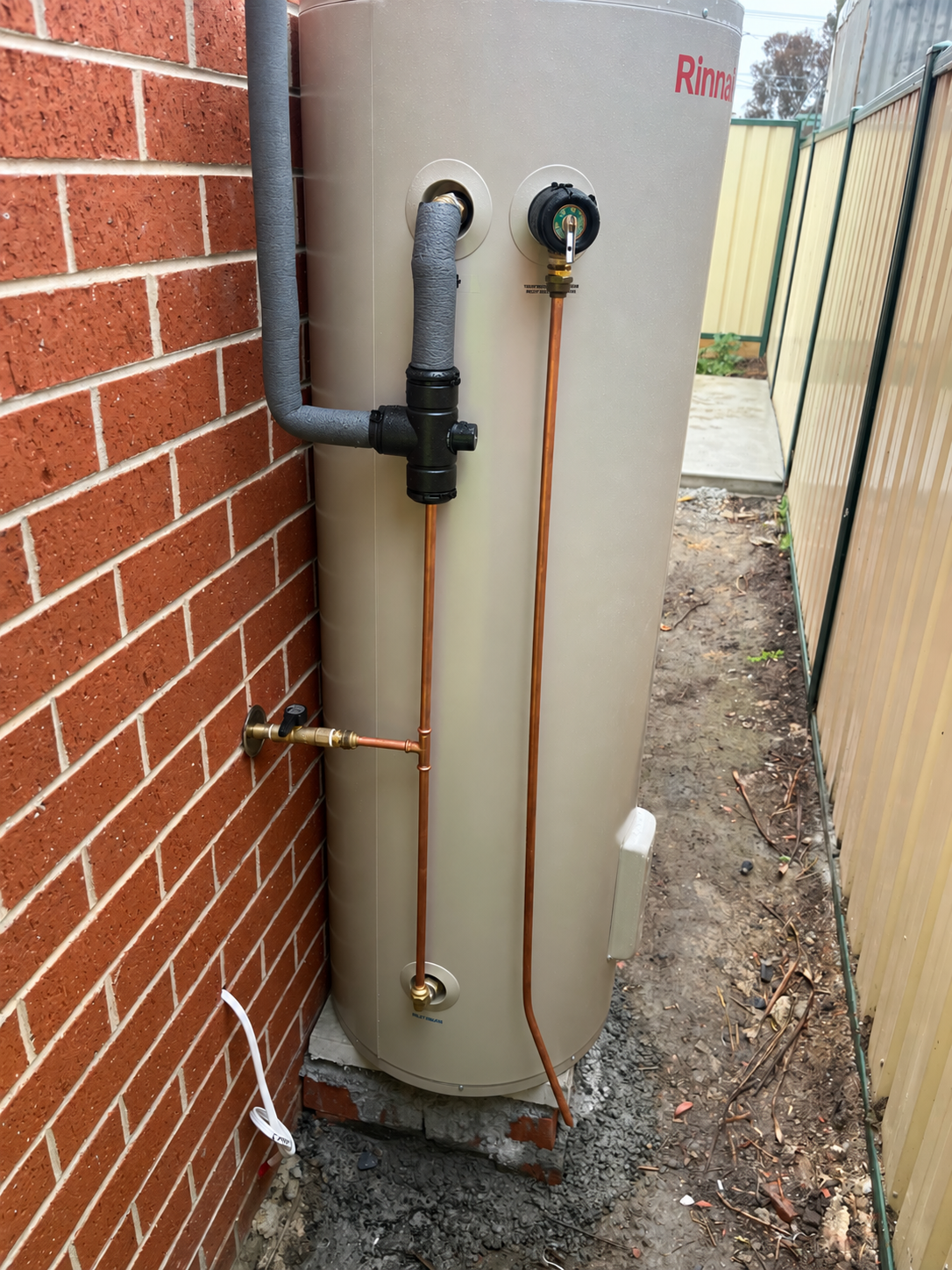 Digitally retouched Rinnai storage hot water system beside a brick wall.